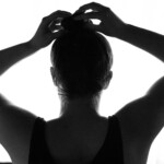 Frau macht sich einen Dutt vor einem Fenster in Schwarz Weiss