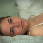 Frau in BH schaut in Kamera und liegt in Bett