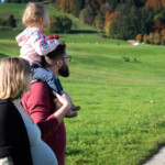 Mutter und Vater mit Kind auf Schultern schauen auf eine Wiese